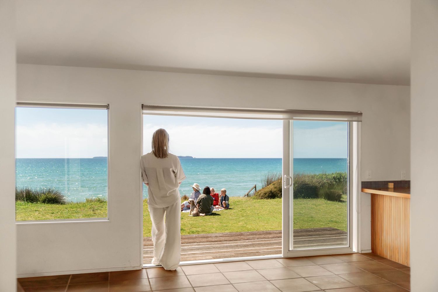 Coastal oceanfront room with sliding glass doors opening to green lawn with turquoise water views.