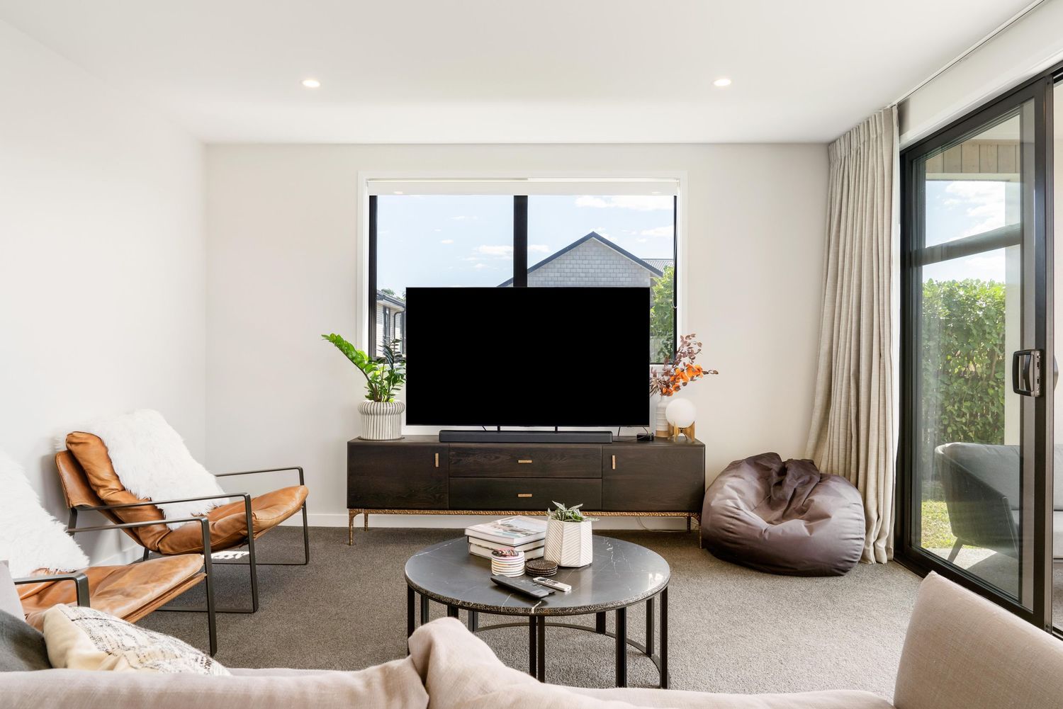 A modern living room with minimalist decor featuring neutral tones, a mounted TV, and large windows with scenic views.
