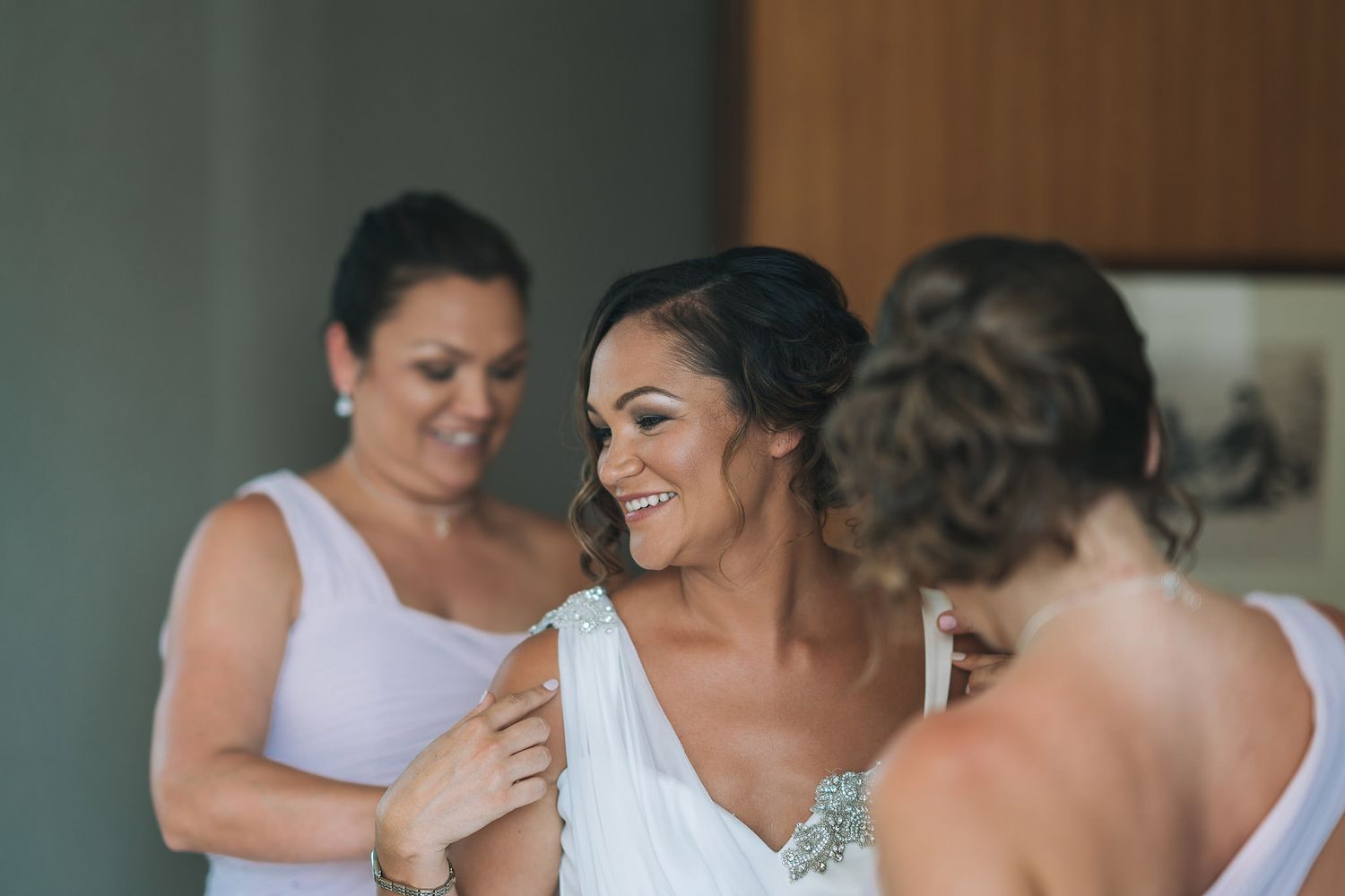 Wedding preparations showing bridal party helping with final dress adjustments in elegant dressing room.