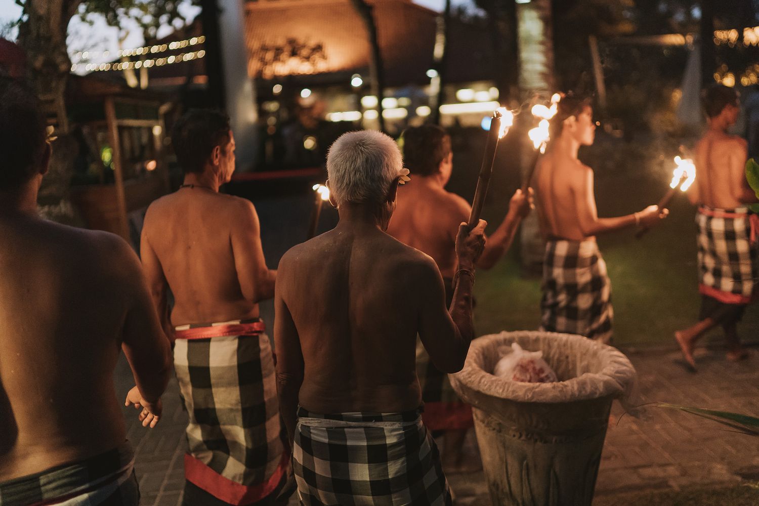 Traditional Balinese performers in sarongs holding torches during an evening cultural ceremony.