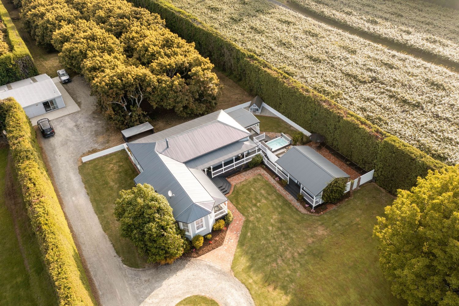 Aerial view of a sun-drenched rural property with lush landscaping and charming cottage-style buildings.