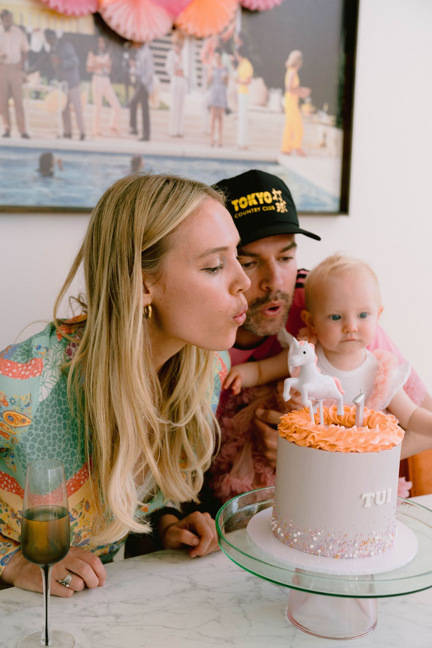 Family gathered around a pink birthday cake with paper decorations hanging overhead.