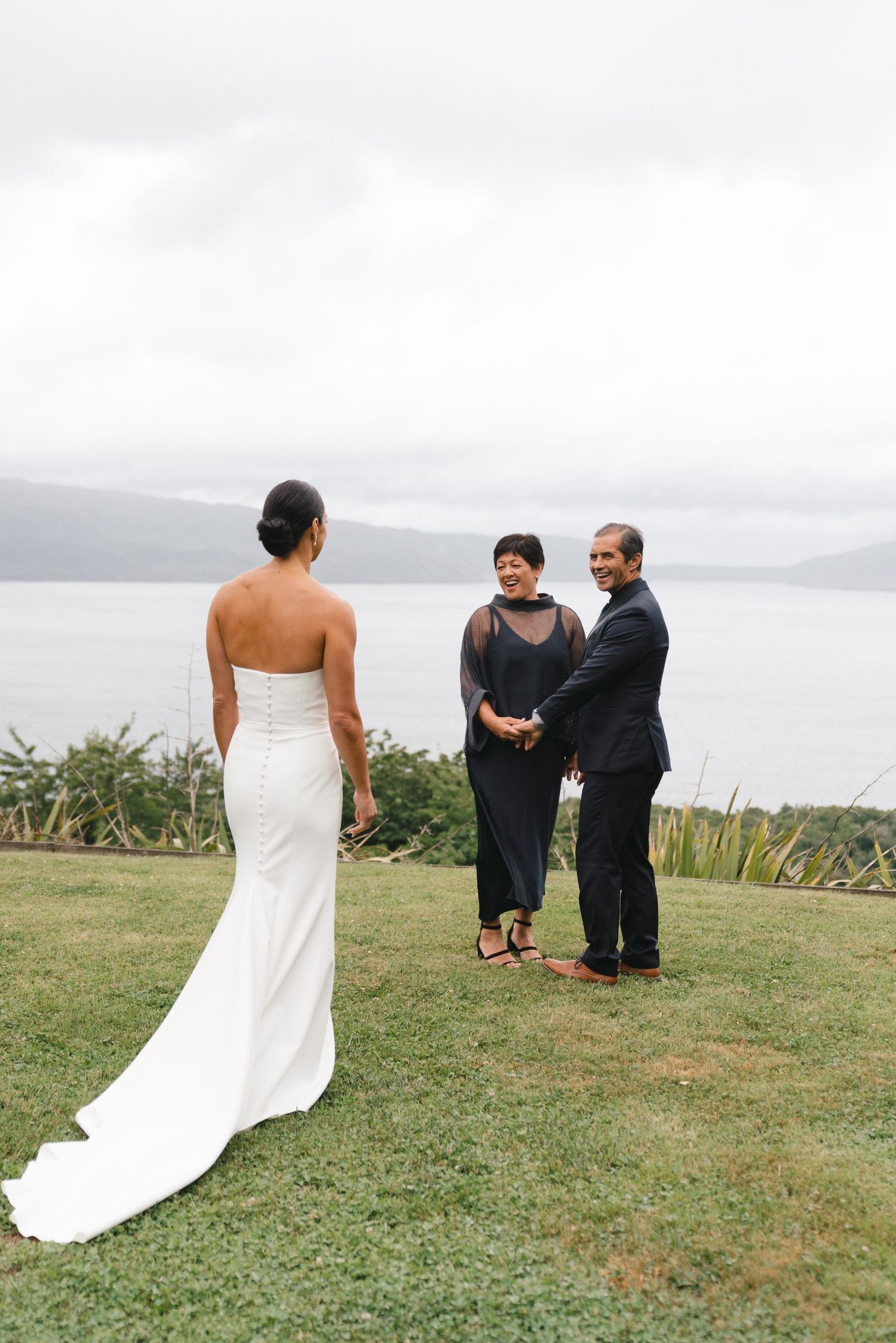 An outdoor wedding ceremony taking place on a grassy cliff overlooking a misty bay.