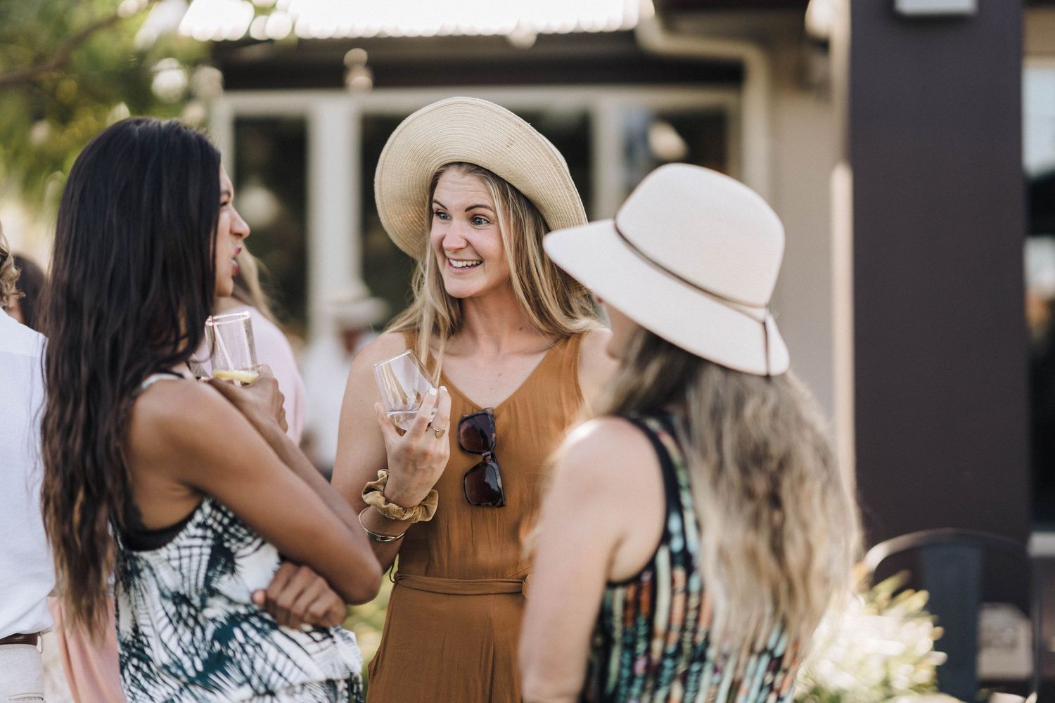Three women chatting and enjoying drinks at outdoor summer party.