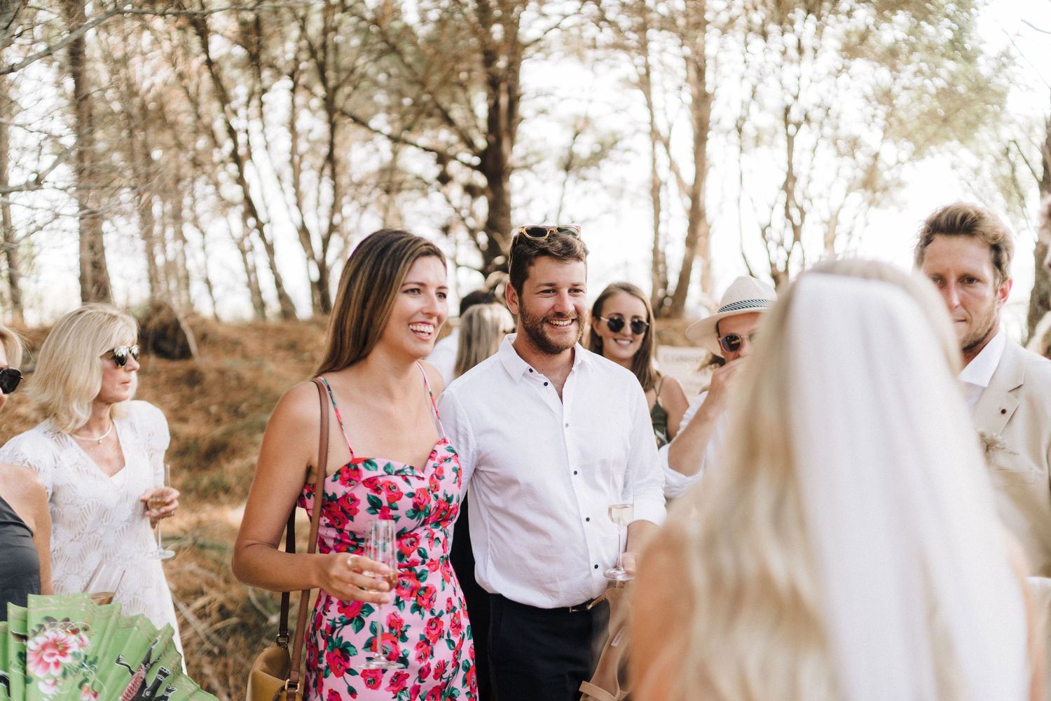 Celebration photos being taken in a wooded area with floral dresses and casual attire.