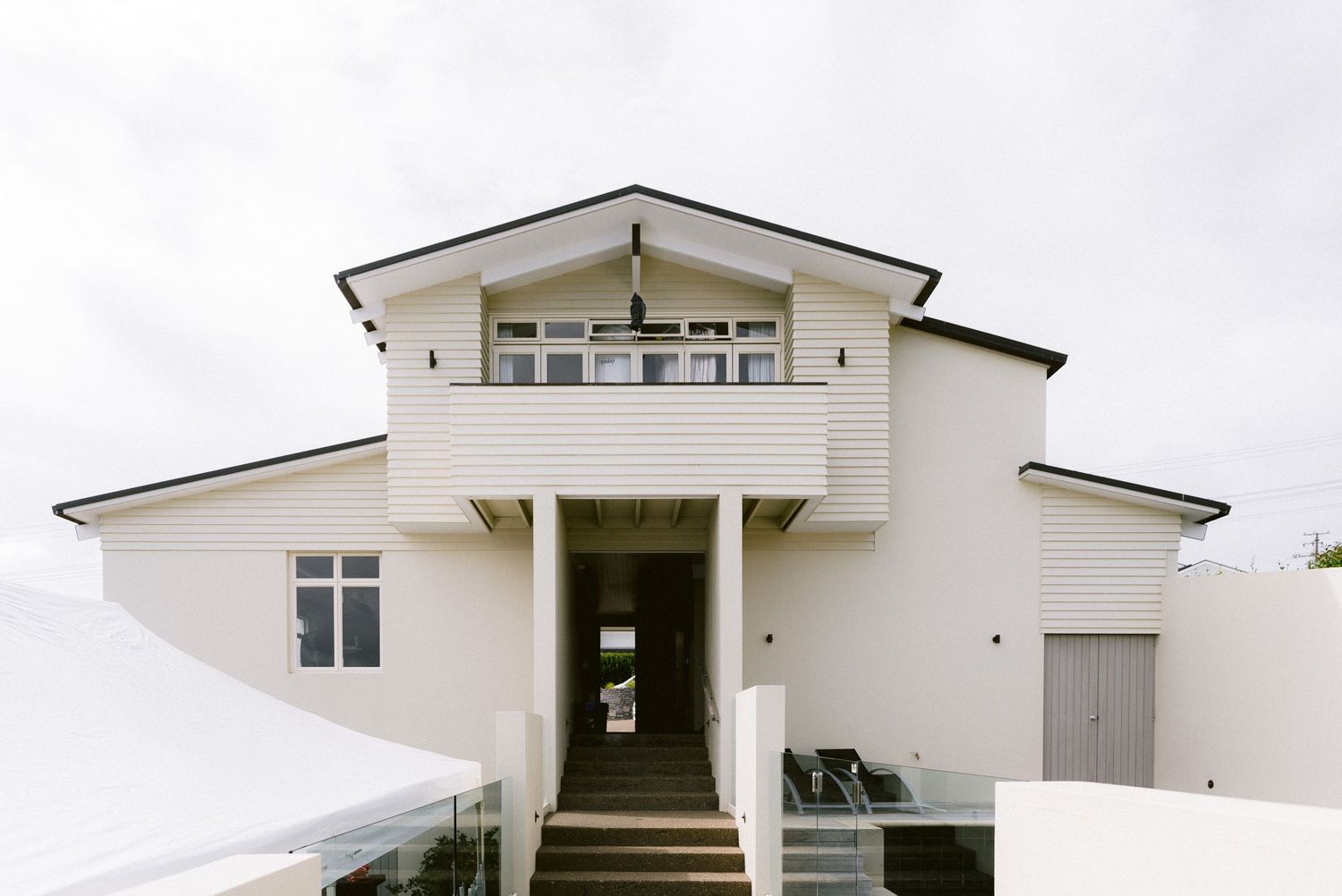 Modern white house with angular architecture featuring a prominent second-story balcony and covered front entrance.