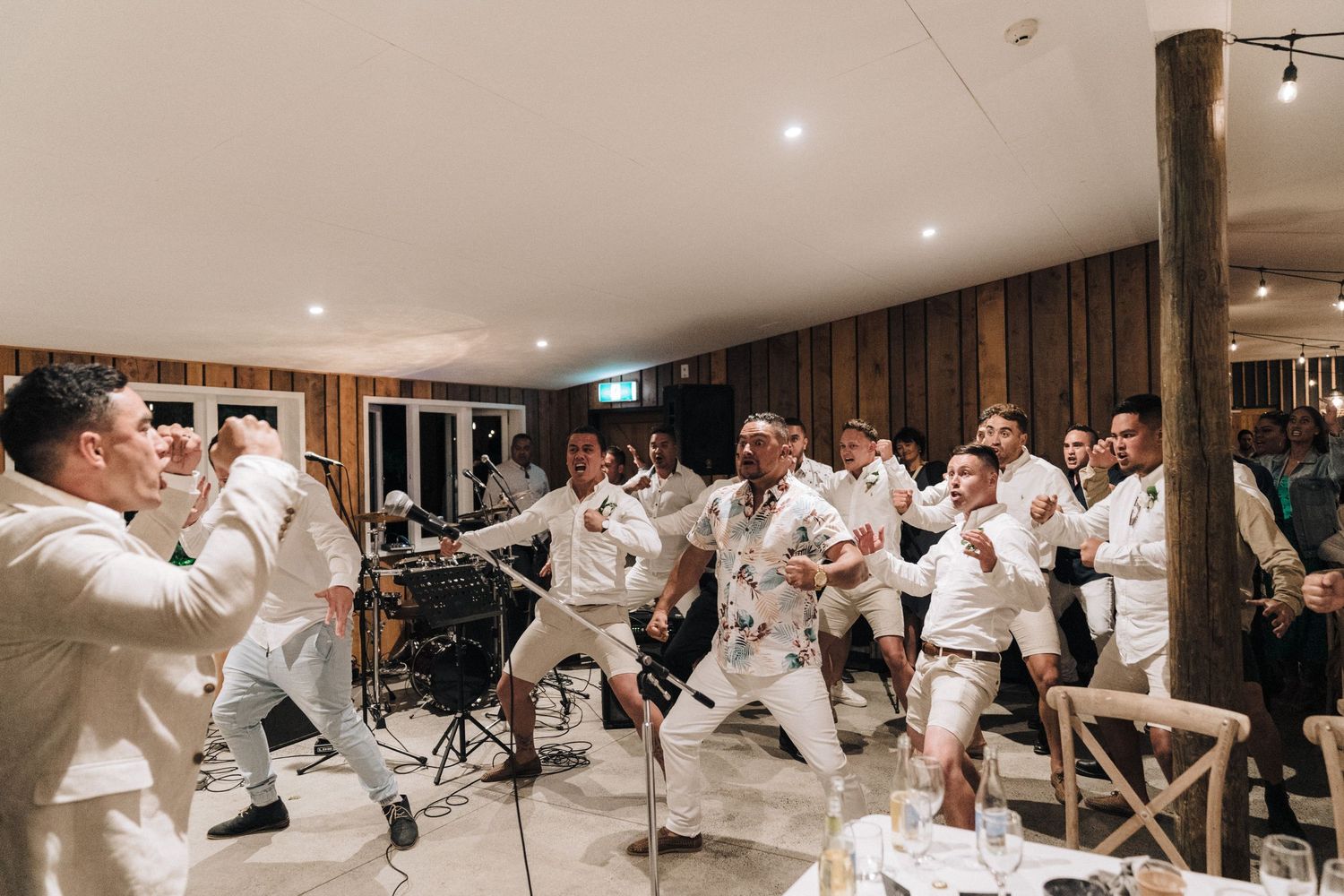 Group of performers in white outfits dancing and celebrating indoors at an event.