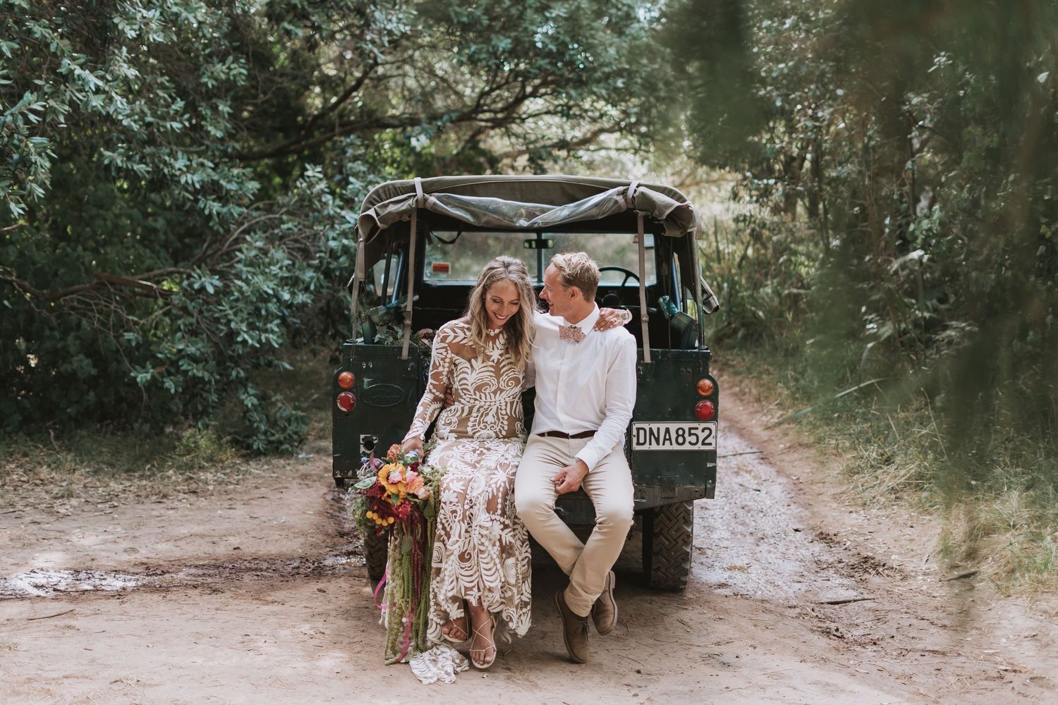 Couple sitting on rustic wooden bench surrounded by lush green forest during romantic outdoor photoshoot.