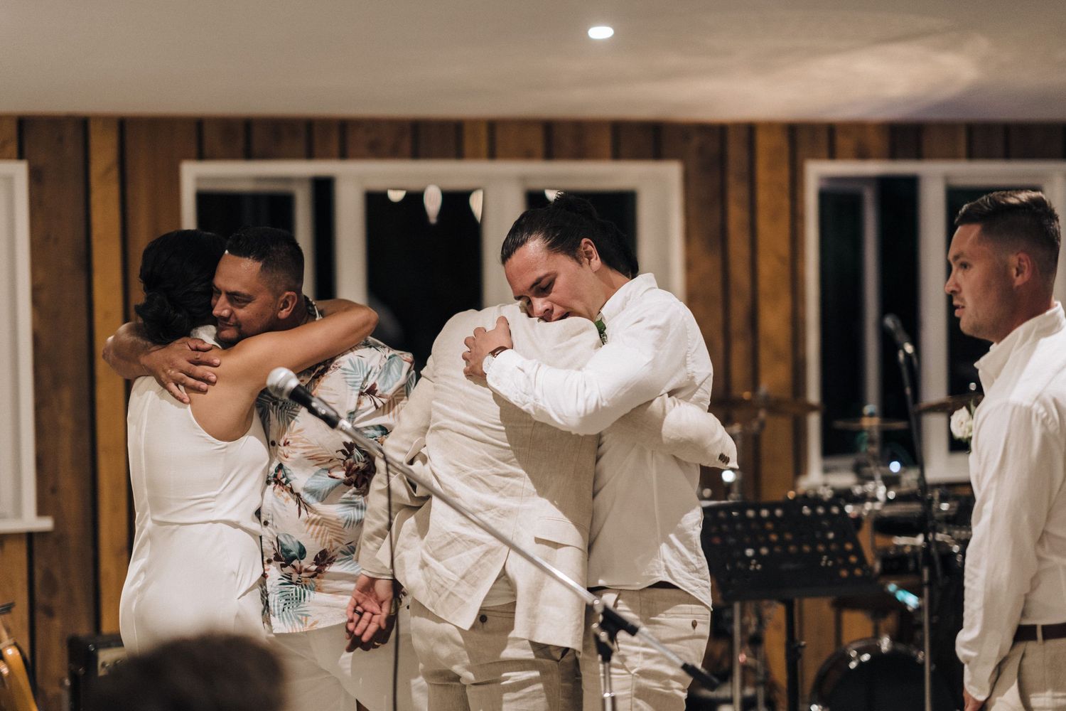 Wedding celebration with joyful dancing and embracing in all-white attire inside a rustic wooden venue.
