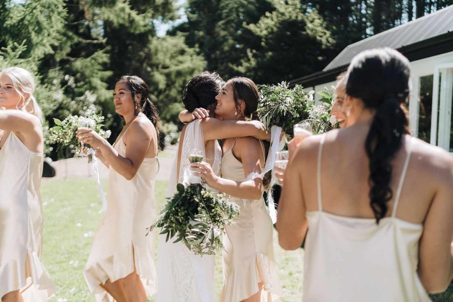 Wedding party dressed in white celebrates together outdoors on a sunny day.