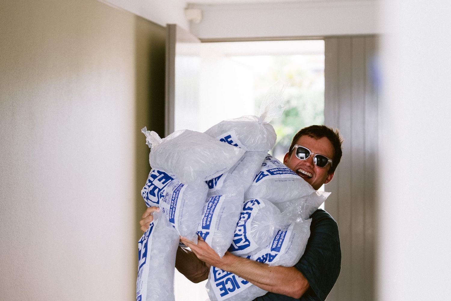 Person in dark shirt carries multiple large packs of Costco brand toilet paper through a narrow hallway.