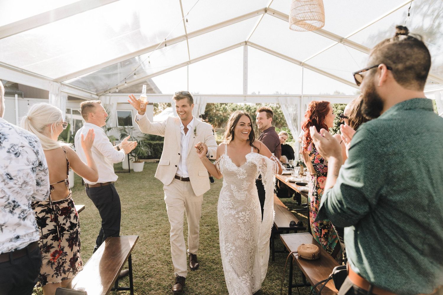 Wedding guests dance and celebrate under an elegant white tent during a festive outdoor reception.