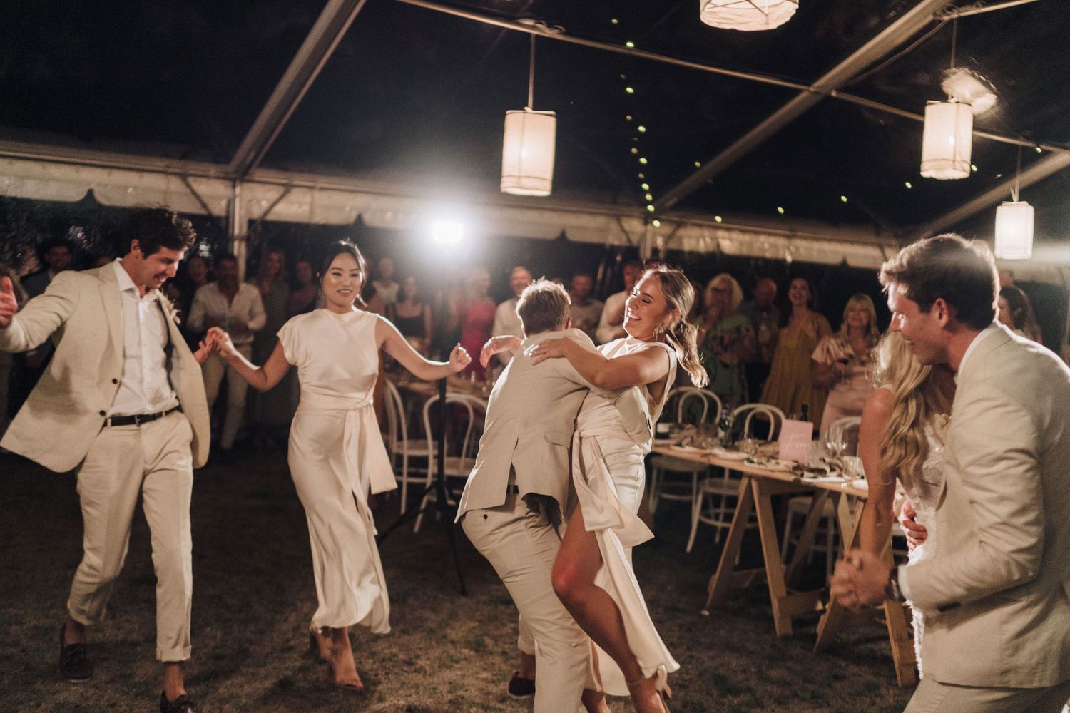 Wedding reception party with guests dancing under hanging lanterns in an outdoor evening celebration.