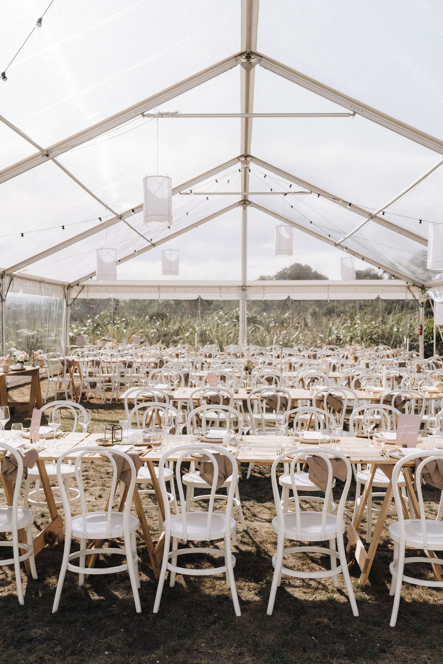 White tent reception venue set up with rustic wooden chairs and tables for an outdoor wedding celebration.