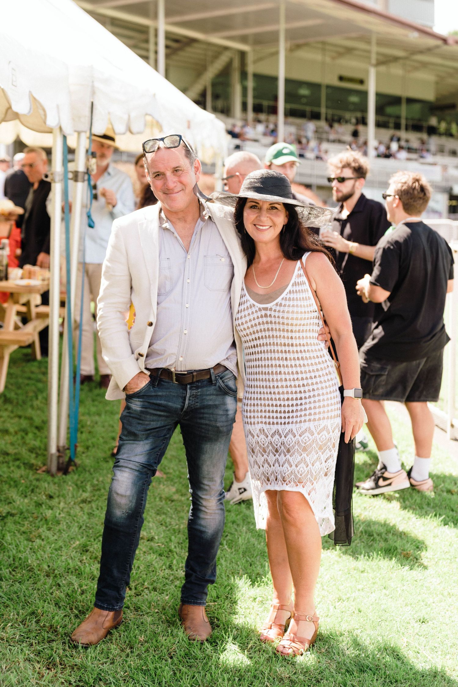 People enjoying a sunny outdoor gathering wearing summer clothing near a white tent.