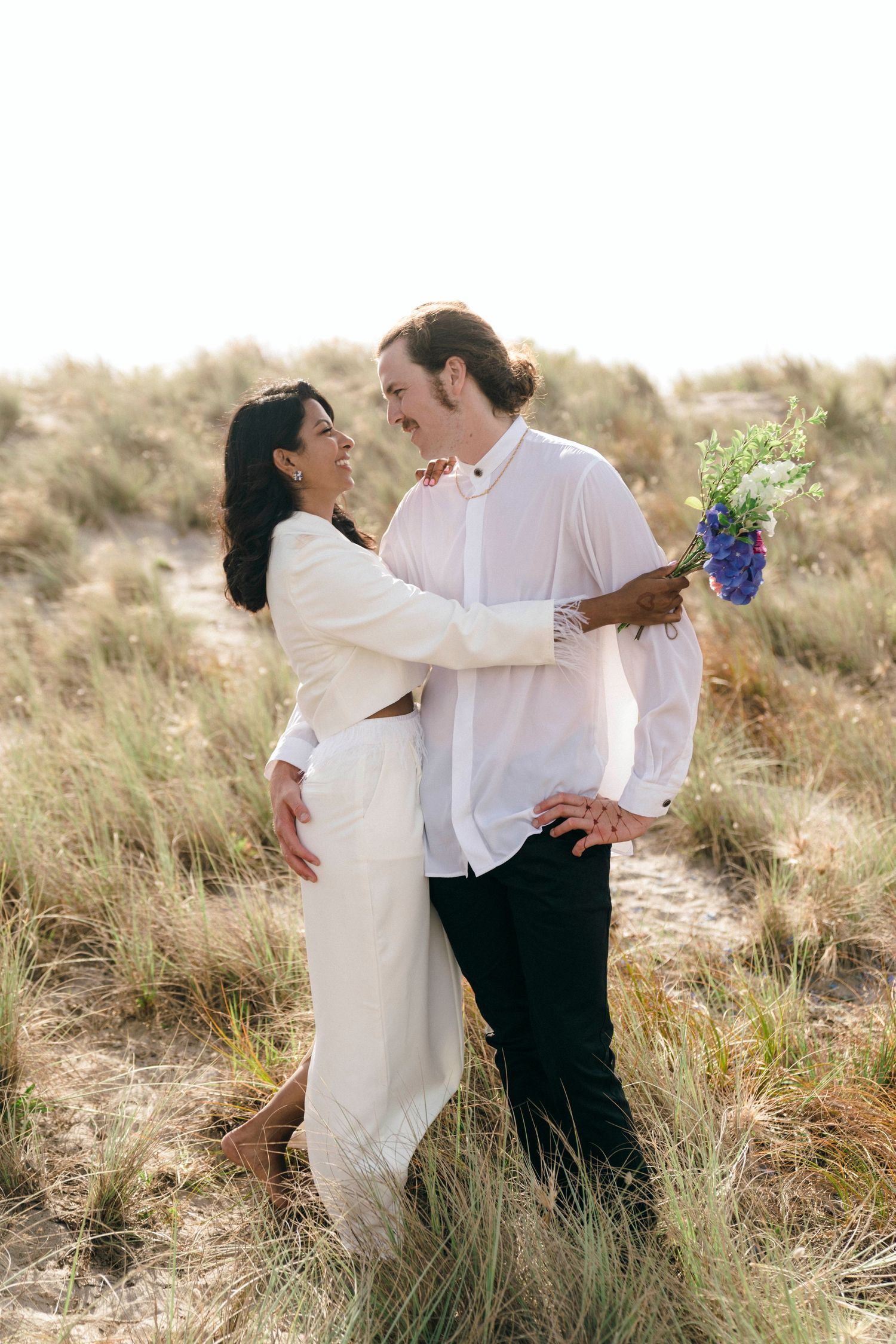 Couple shares intimate romantic moment among coastal grasses with ocean view.