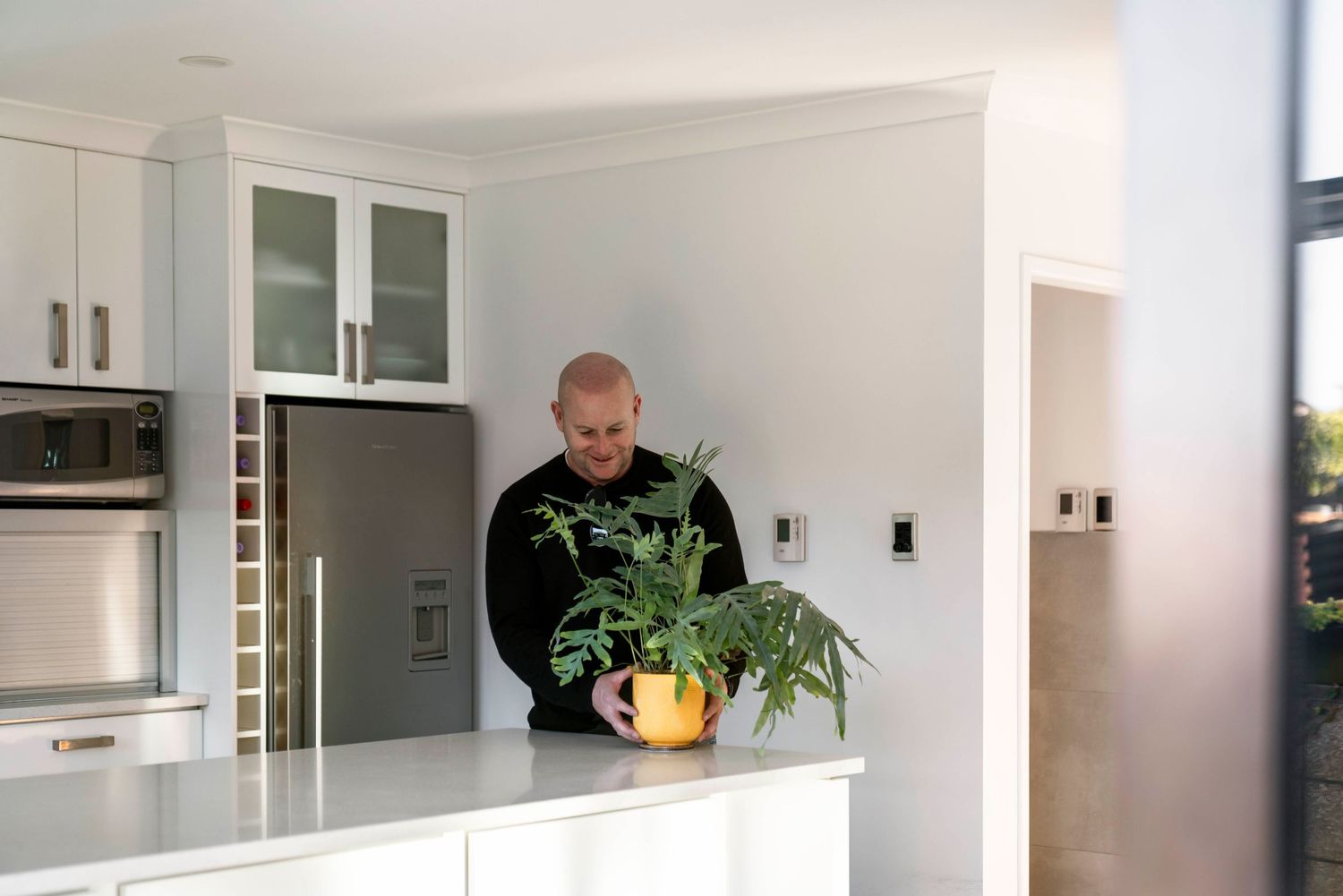 Modern white kitchen interior with glass-front cabinets and person holding fresh produce.
