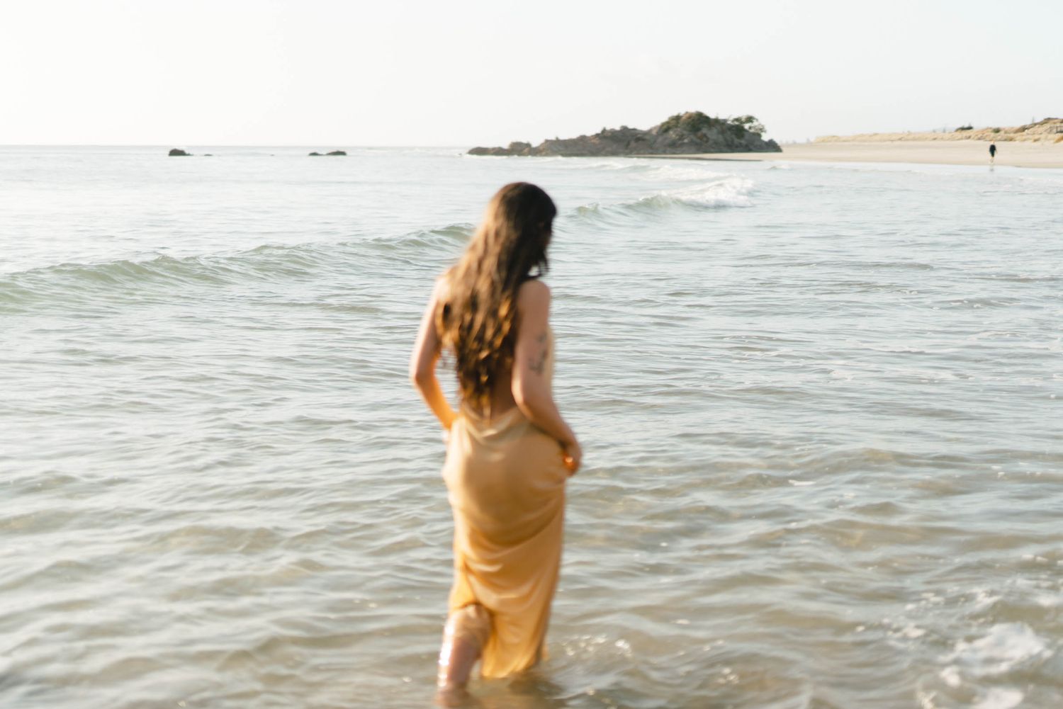 Person wades through gentle ocean waves during a sunset beach photoshoot.