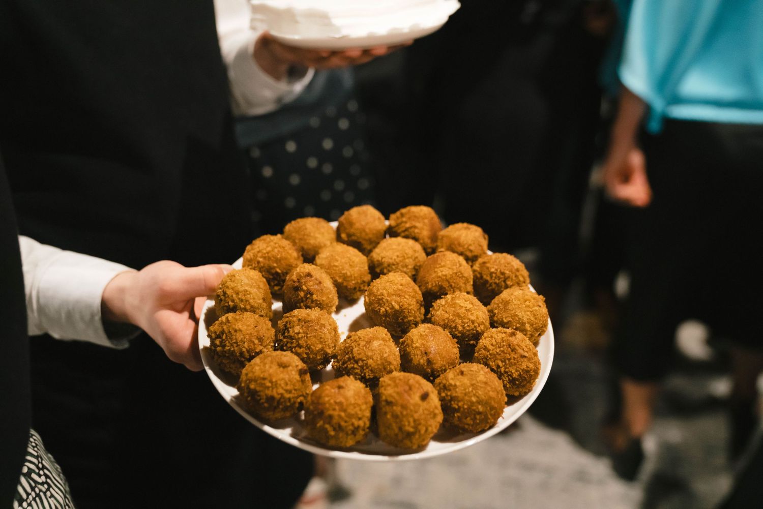 A plate full of golden-brown breaded appetizers or croquettes being served at an event or gathering.