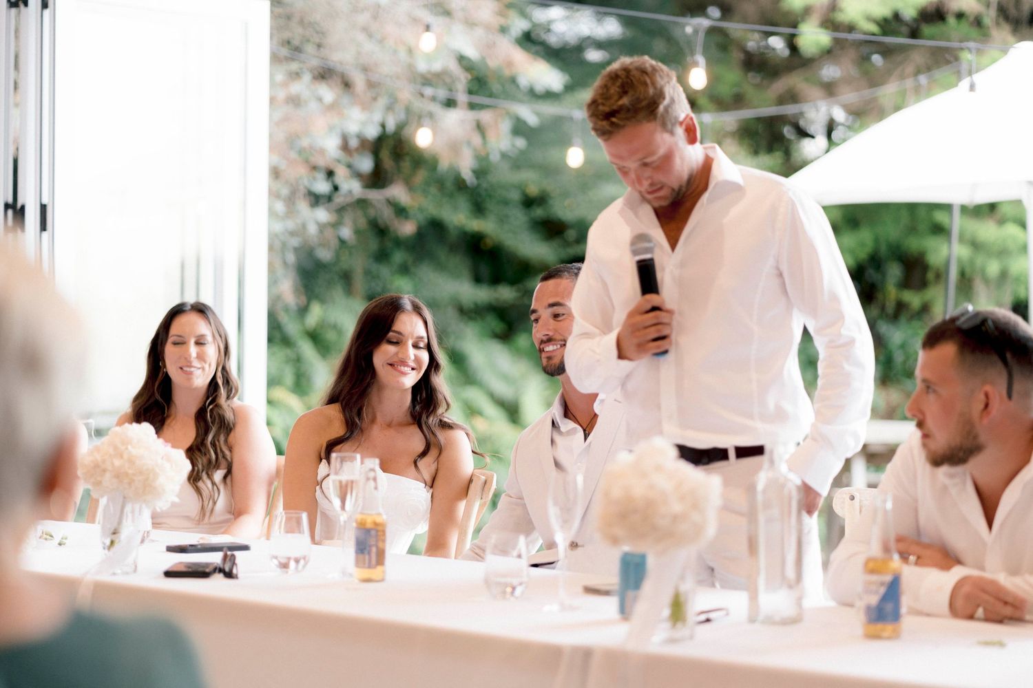 Wedding guests enjoying drinks and conversation at outdoor tables during reception.