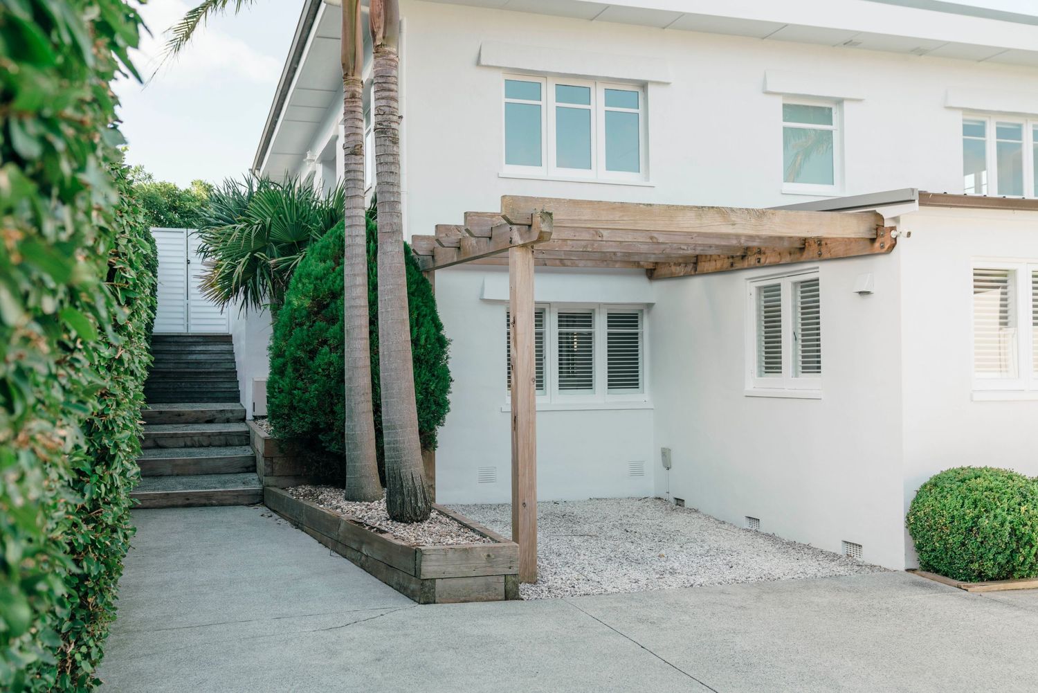 White house exterior with wooden pergola, stone steps, and manicured hedges.