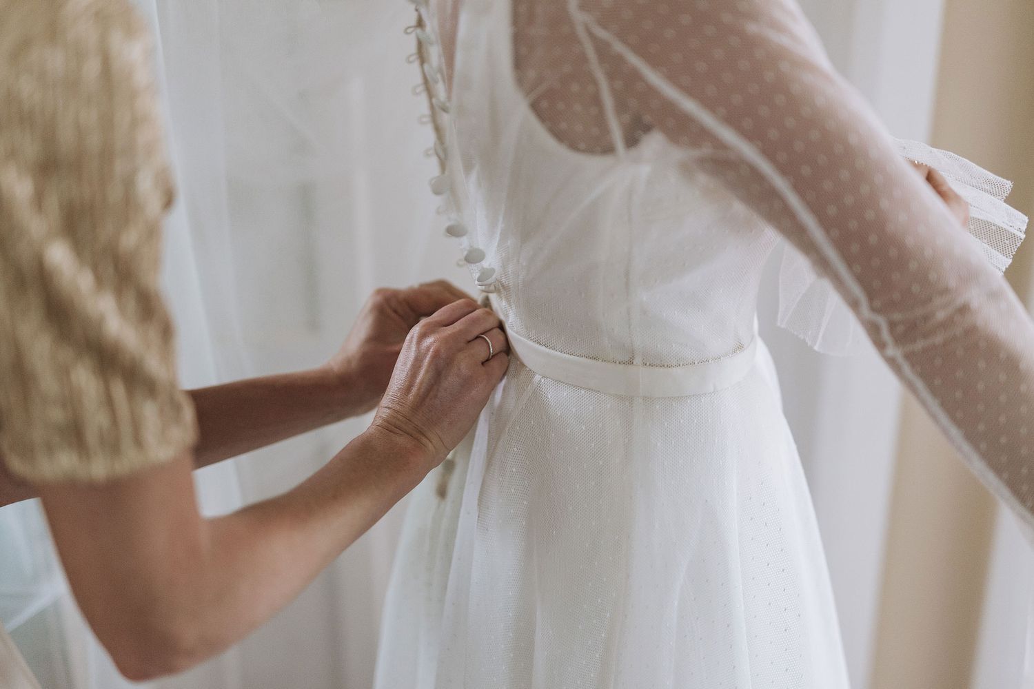 A flowing white dress with delicate lace details is shown in a soft natural light setting against a neutral background.