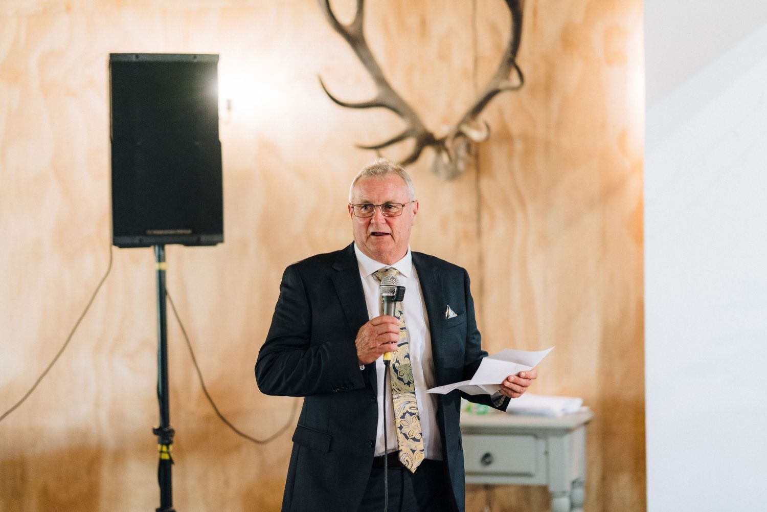 A speaker delivers remarks at an elegant wedding reception with warm lighting.
