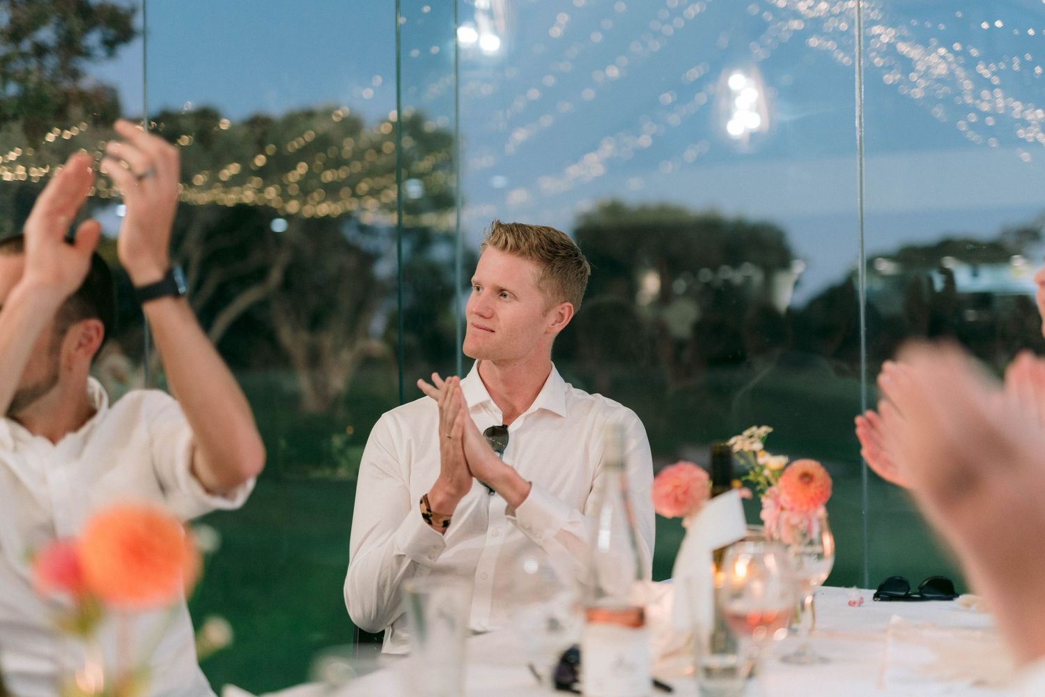 A wedding celebration at dusk under string lights with guests gathered around outdoor dining tables.