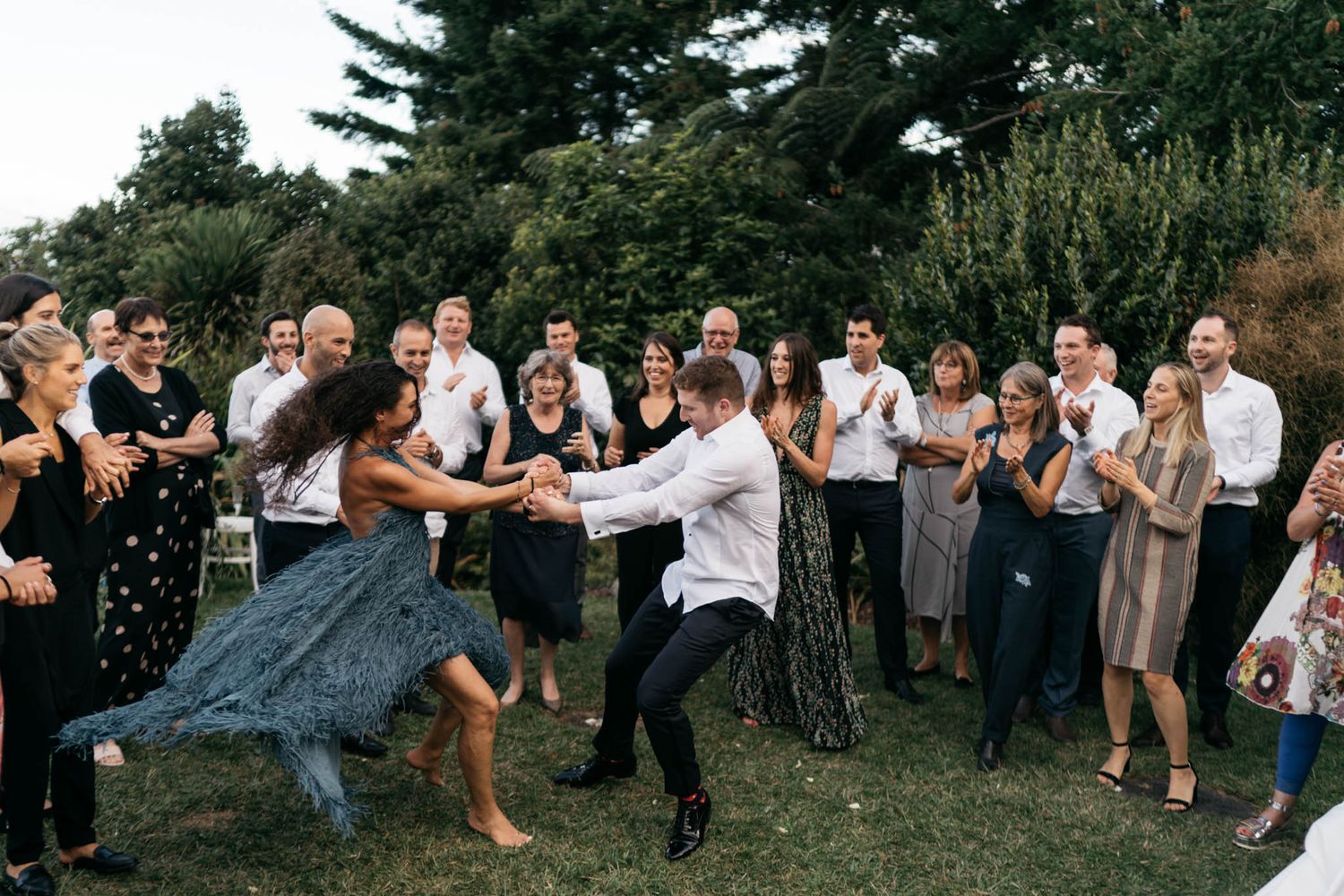 Wedding guests cheer as couple pops champagne in an outdoor garden celebration.