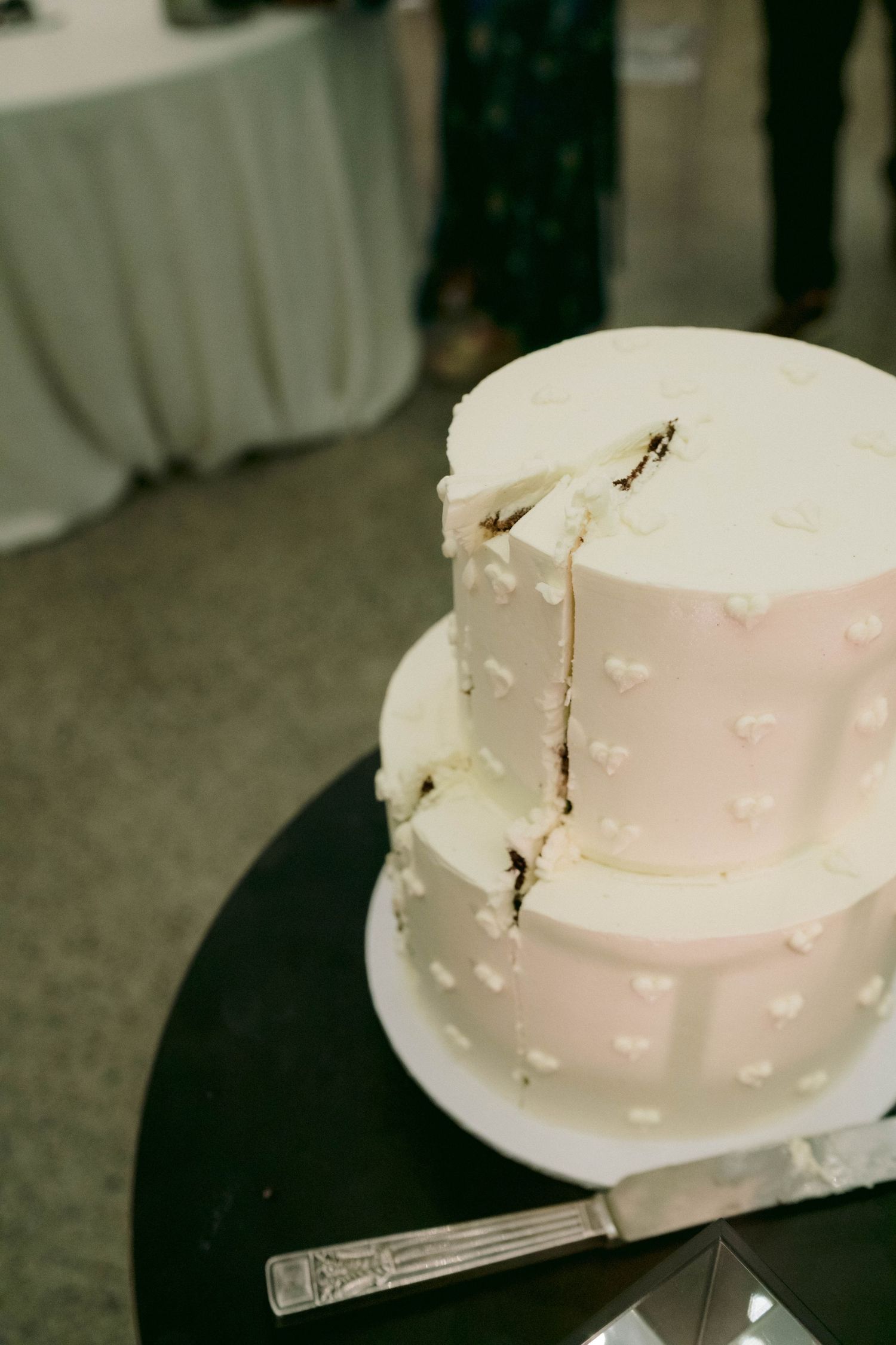 Close-up of white wedding cake with delicate heart pattern details being cut.