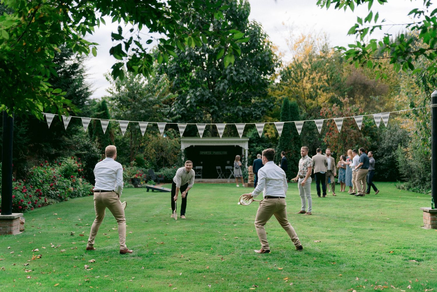 Wedding guests playing lawn games under string lights in a garden setting.