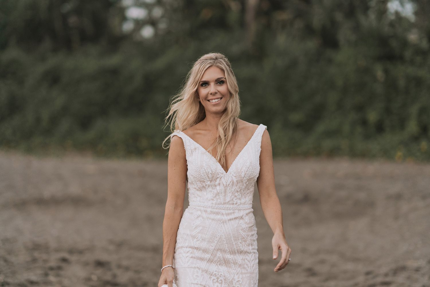 Bride in white lace dress poses gracefully in an outdoor garden setting.