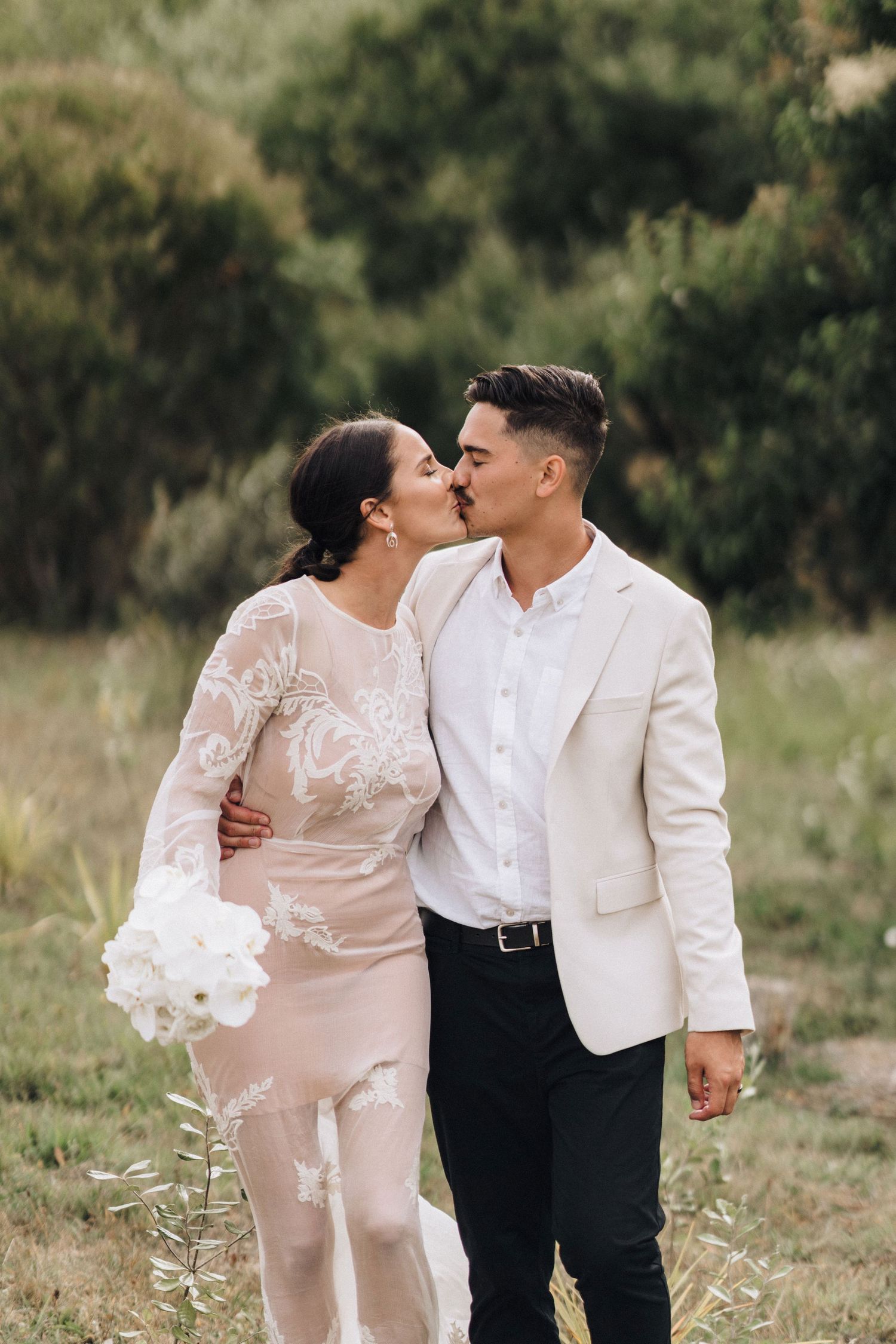 A romantic outdoor photoshoot in a grassy field with a couple wearing white formal attire.