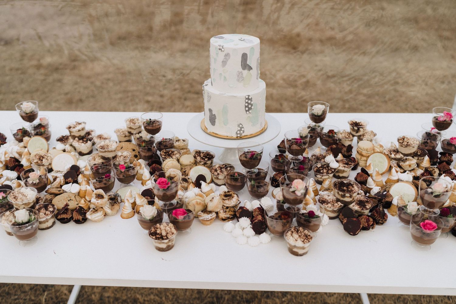 A display of chocolate desserts and treats arranged around a white wedding cake on a long table.