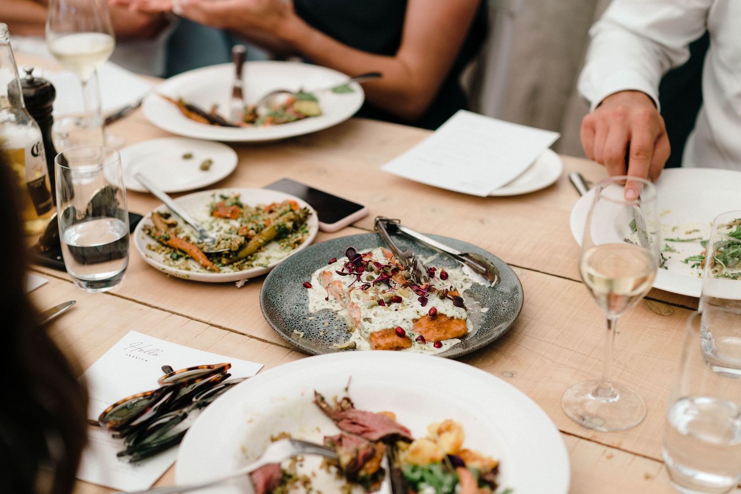 Multiple elegantly plated dishes are served on a dining table with wine glasses and modern restaurant ambiance.