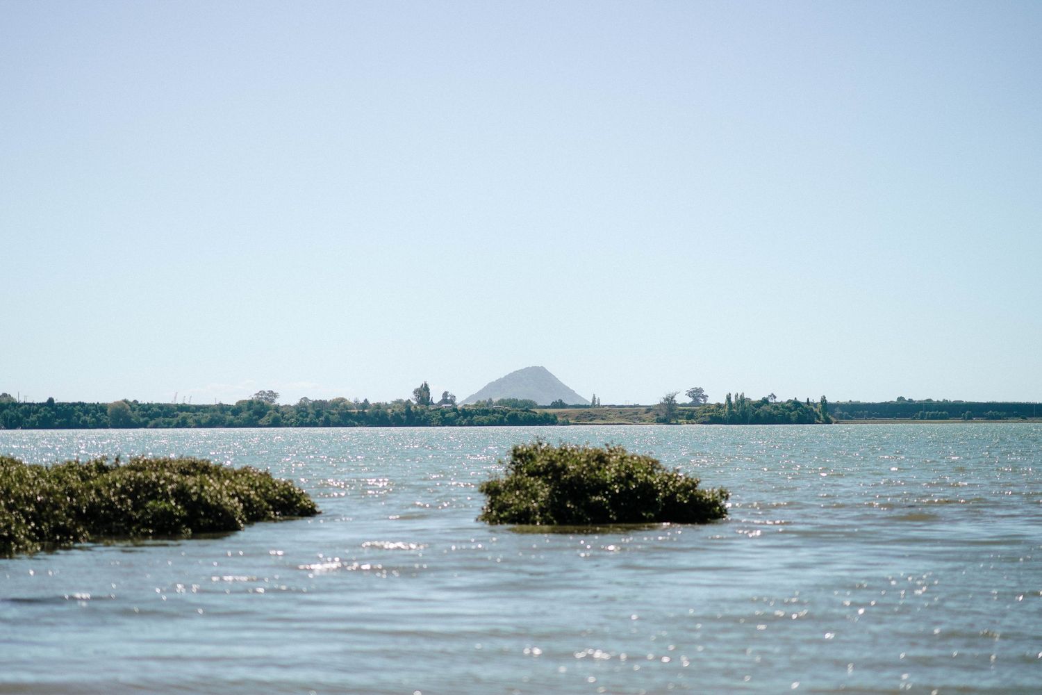 Serene lake landscape with small islands and mountain silhouette under blue sky.