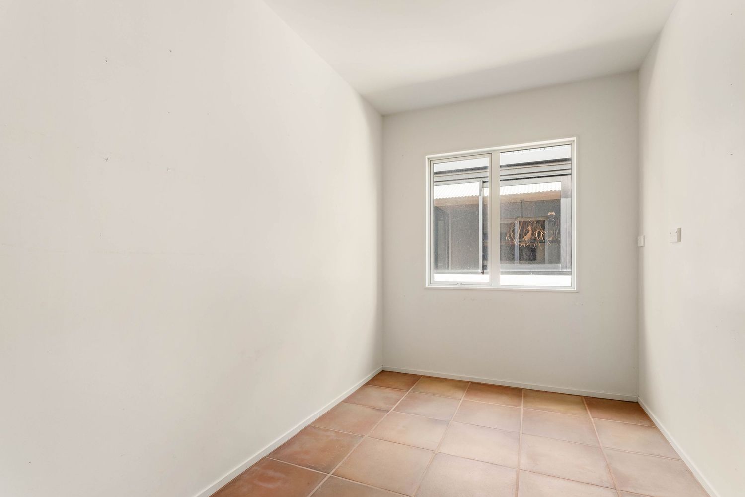 Empty room with white walls, window, and terracotta floor tiles.