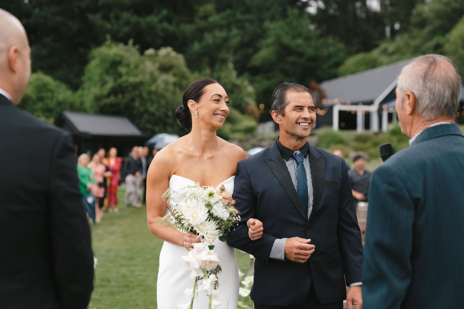 Wedding guests gather on a lush green lawn to celebrate during an elegant outdoor summer reception ceremony.