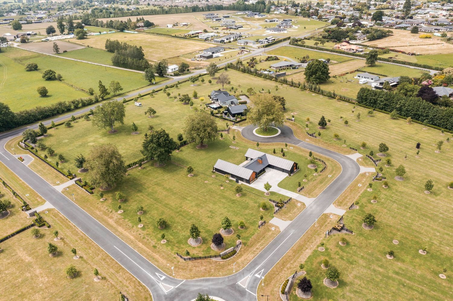 Drone shot of luxury property with circular driveway surrounded by manicured lawns and rural landscape.