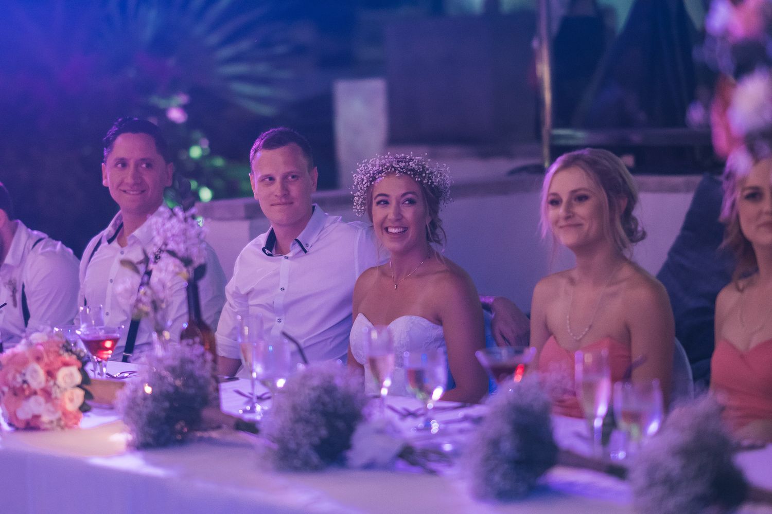 Wedding reception venue illuminated in purple lighting with guests seated at decorated tables.