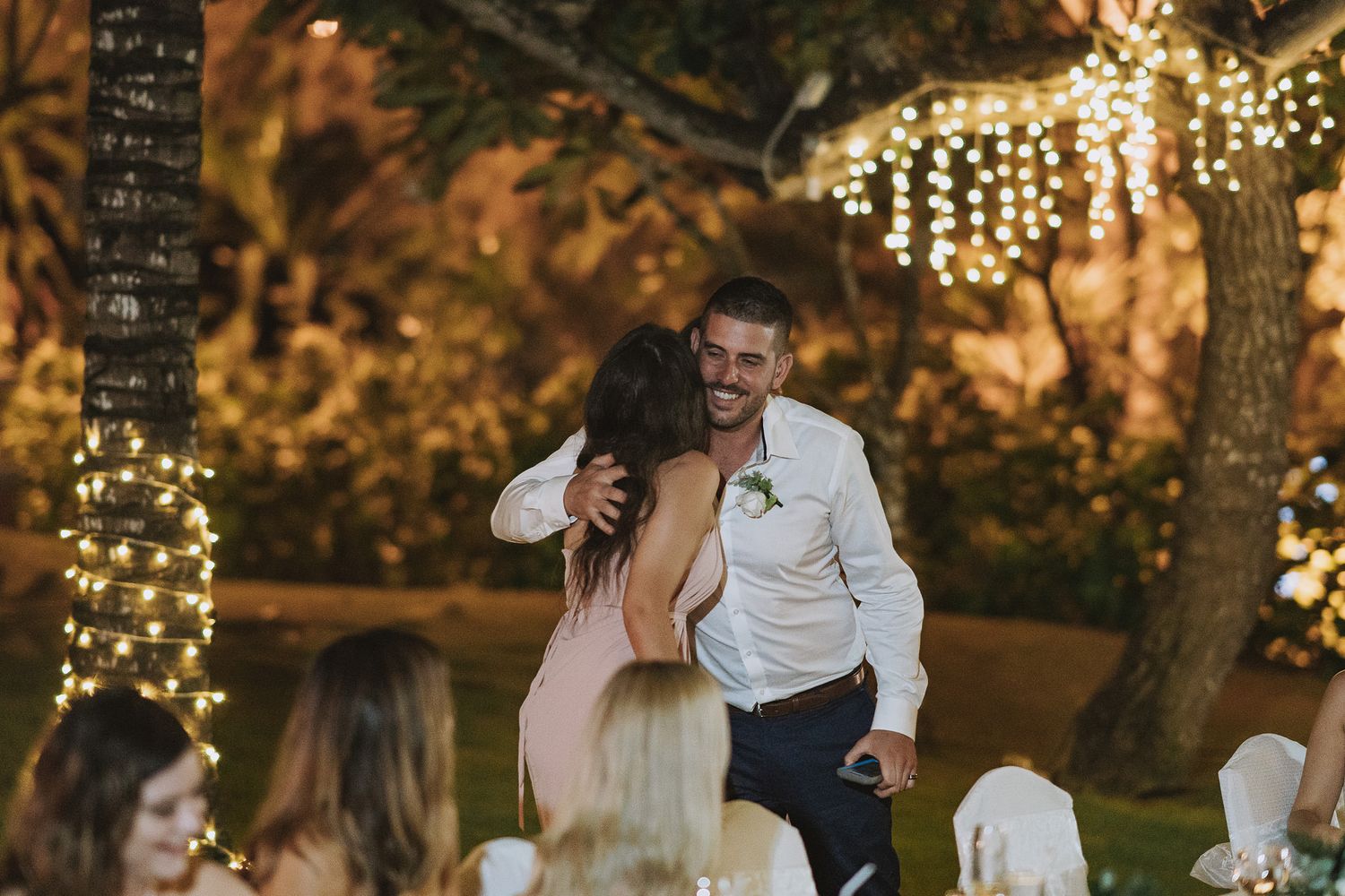 Joyful celebration moment at outdoor wedding reception with string lights in trees.