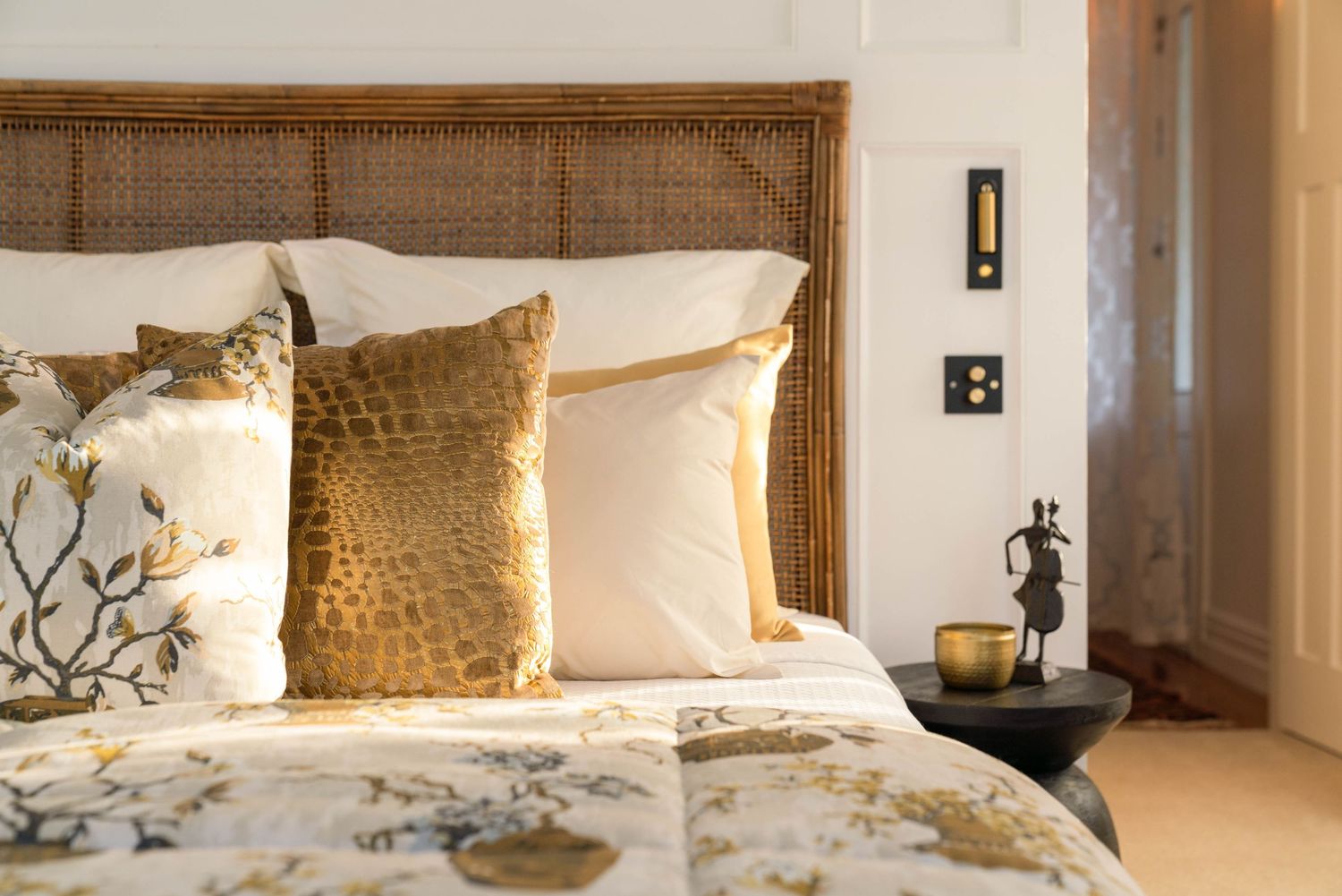 Cozy bedroom with rattan headboard, gold accent pillows and floral bedding.
