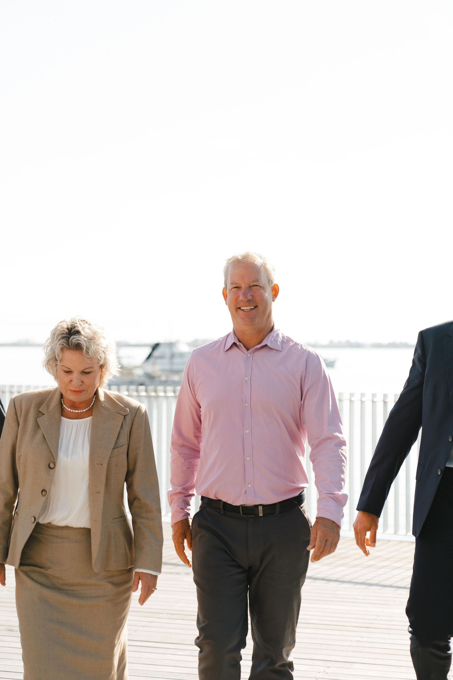 Business professionals walking together on a bright outdoor deck near a waterfront railing.
