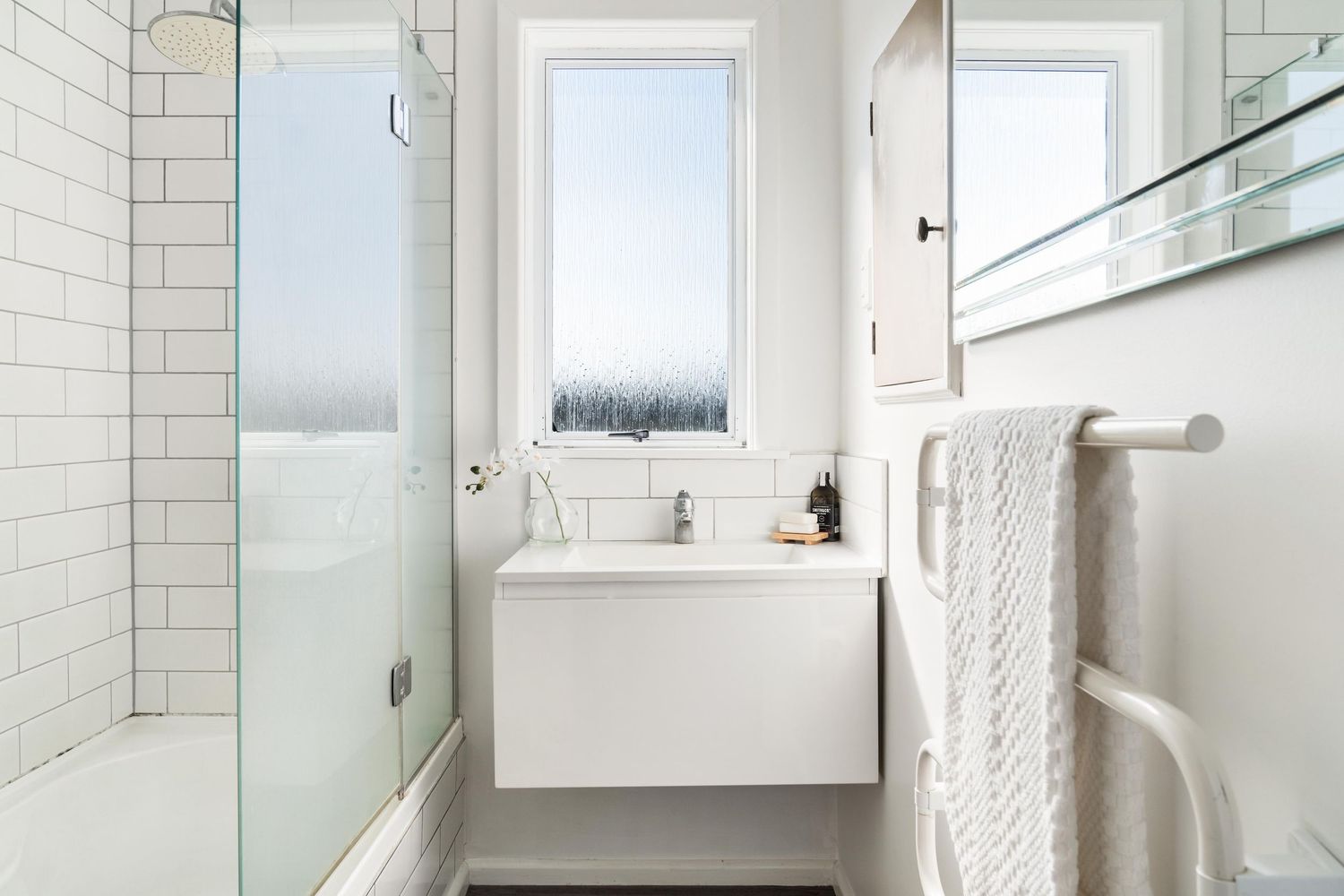Bright white bathroom with subway tiles, glass shower enclosure and large window providing natural light.
