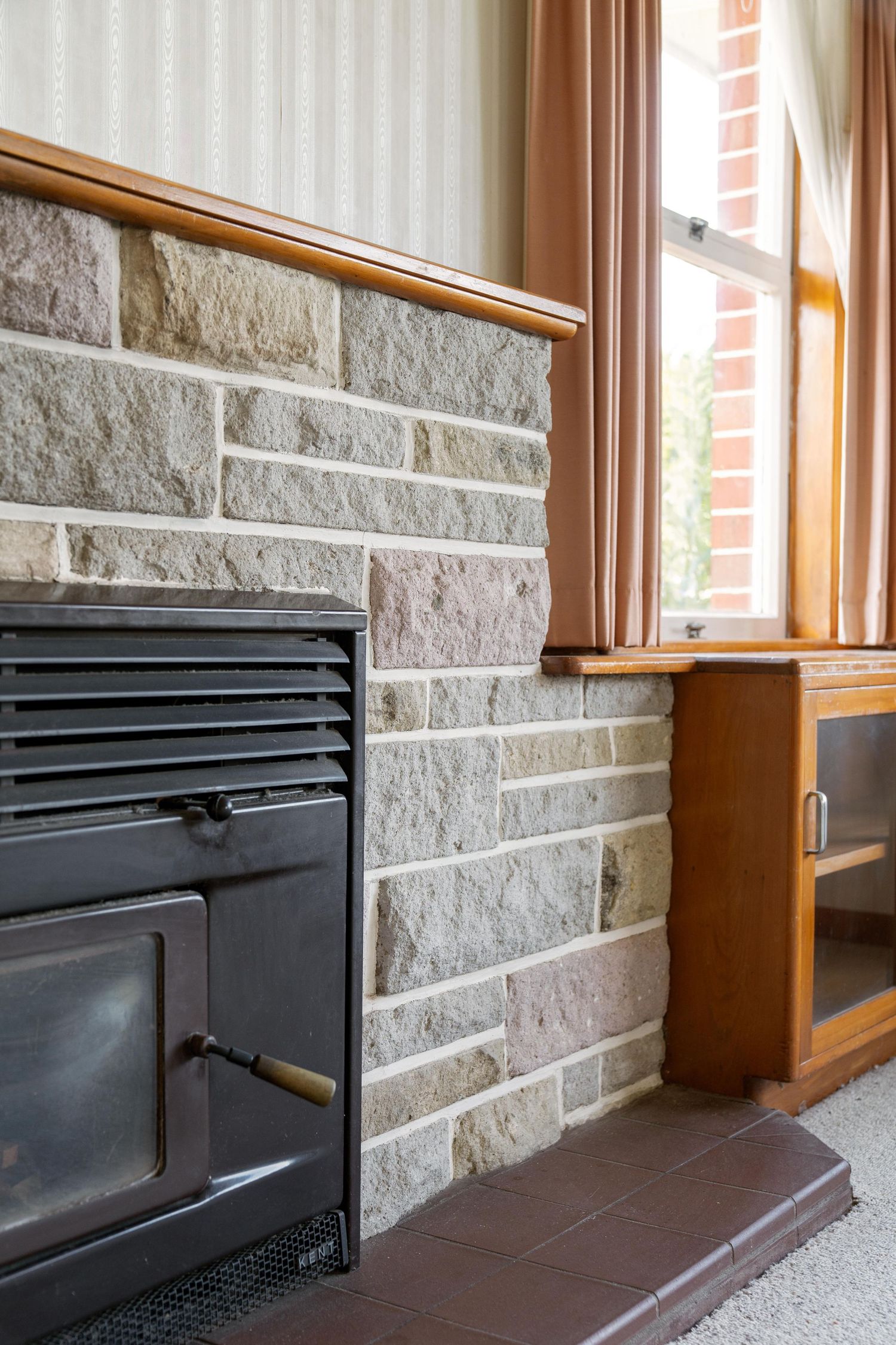 Four connected photos showing a black fireplace insert installed against a textured stone wall with wooden window trim.