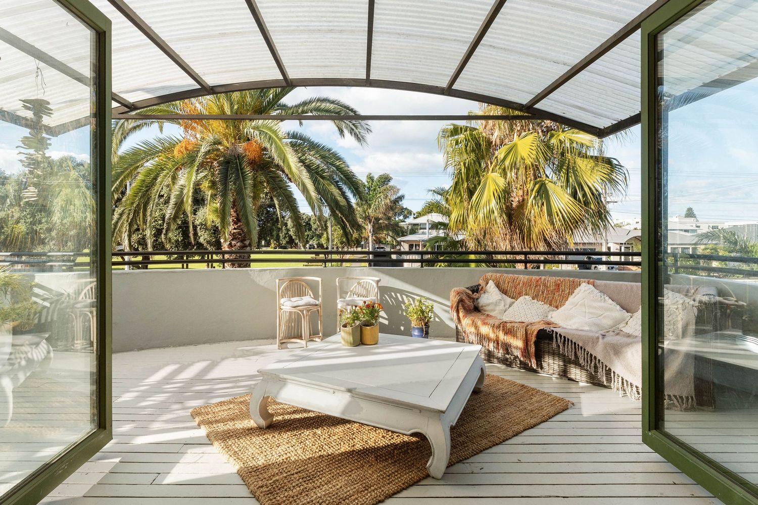 Luxurious covered outdoor deck with loungers and palm tree views.