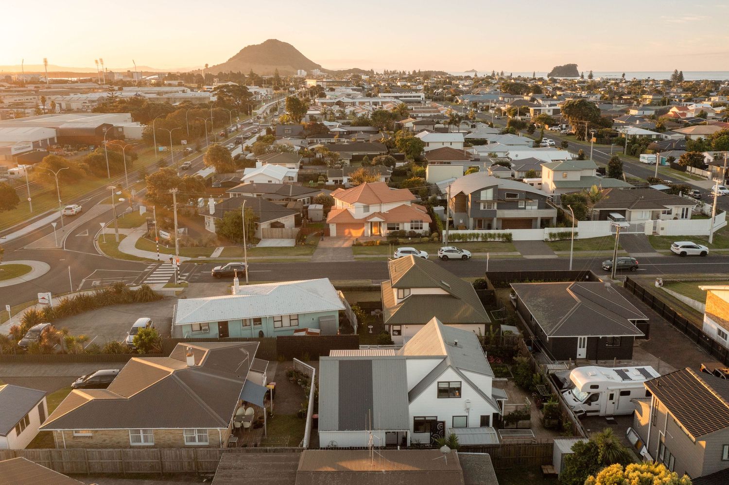 Aerial view of suburban neighborhood in New Zealand with Mount Maunganui visible in the golden sunset light.