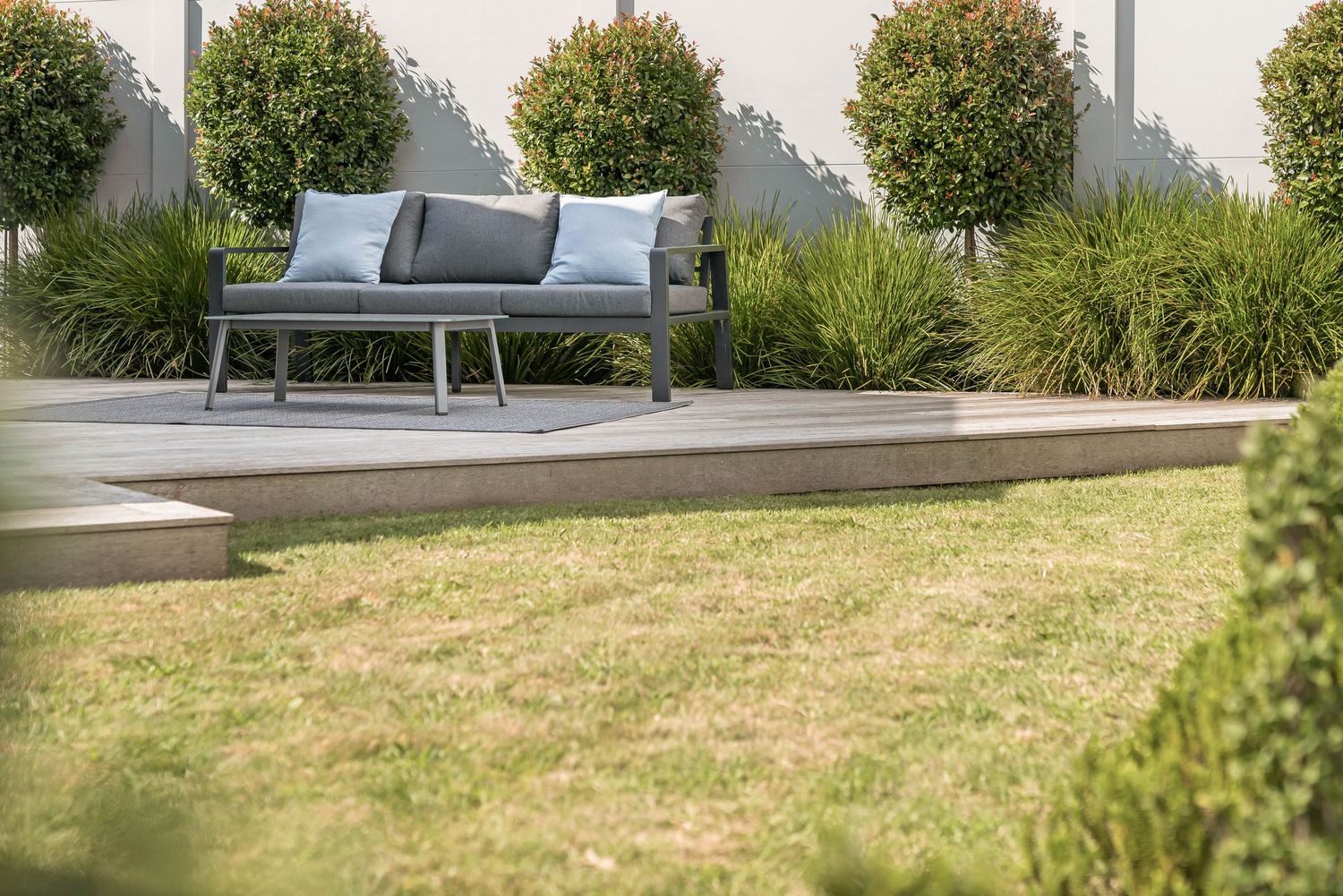 Outdoor gray lounge sofa on concrete patio surrounded by manicured garden and trees.