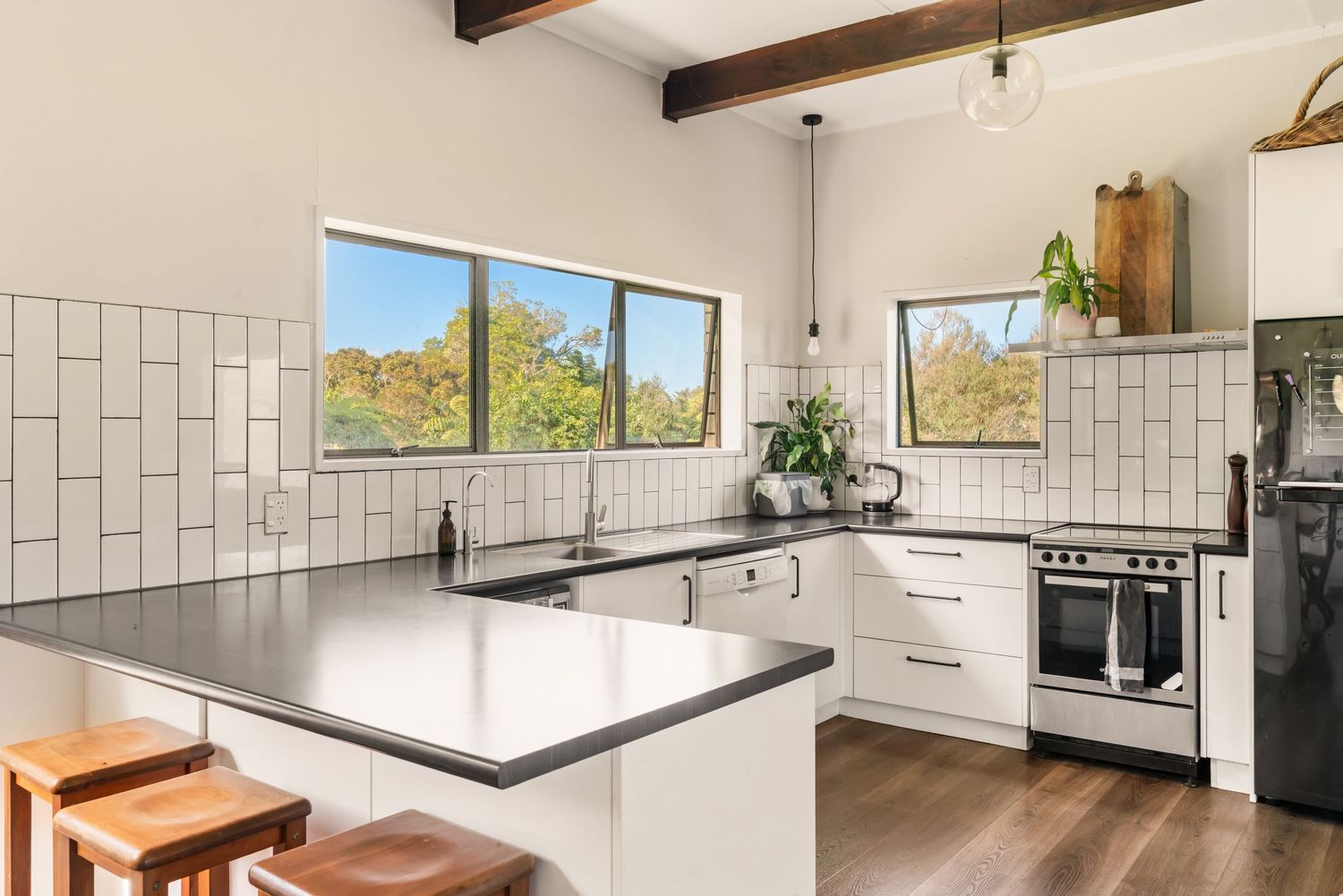 Modern white kitchen with stainless steel appliances, U-shaped counter layout and wooden bar stools under natural lighting.
