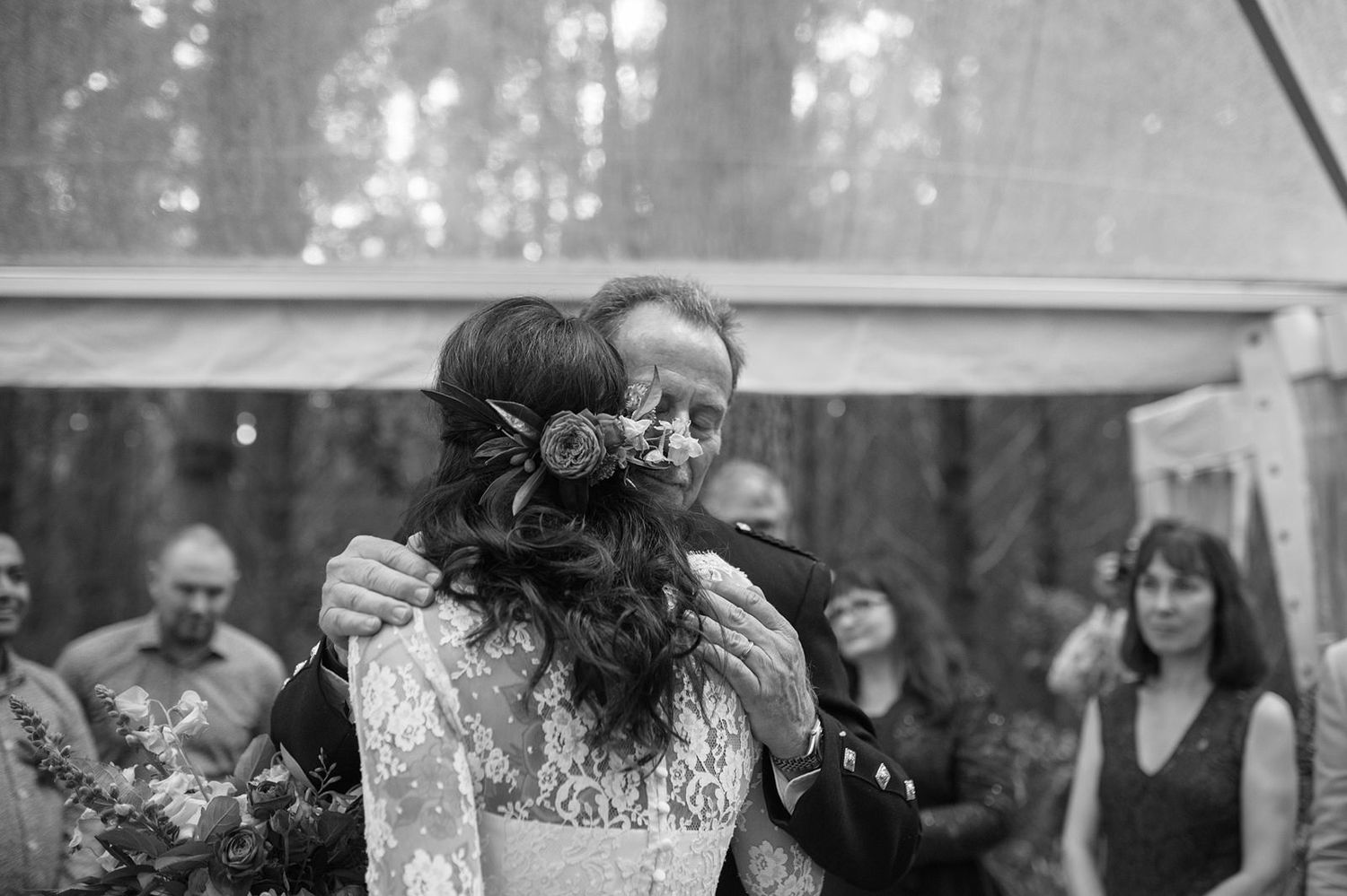 An intimate black and white moment showing a celebratory embrace at an outdoor wedding reception.